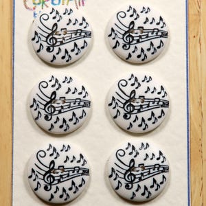 May include: Six white, round buttons with a black musical note design. Each button features a treble clef, musical staff, and scattered quavers. The buttons are attached to a cream-coloured card.