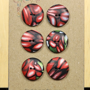 May include: Six round buttons with a marbled design in red, black, white, and green. Each button has two holes for sewing. The buttons are arranged on a brown cardboard surface.