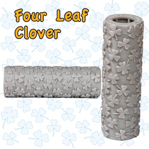Può includere: Due rulli per goffratura cilindrici grigi con un motivo a quadrifoglio. Il testo "Four Leaf Clover" è visualizzato in giallo e blu. I rulli sono progettati per creare motivi strutturati.