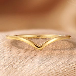 May include: A polished yellow gold ring featuring a V-shaped chevron design. The band has a smooth, continuous metallic surface that tapers to a point at the center. The ring is displayed with the text Nobel Yates Fine Jewelry visible.