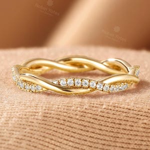 Op de afbeelding: Een gouden ring met een gedraaid bandontwerp. Eén streng van het gedraaide metaal is bezet met kleine, heldere, rondgeslepen stenen, terwijl de andere streng bestaat uit gepolijst, glad goudmetaal, wat een doorlopend, verweven patroon creëert.