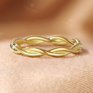 May include: A polished gold ring featuring a continuous twisted rope design. The band is crafted from a single piece of metal that loops over itself to create a braided, intertwined appearance with a smooth, reflective surface finish.