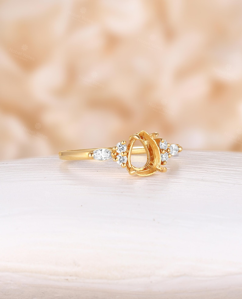 May include: A gold ring setting with a pear-shaped center stone and small round and pear-shaped accent stones.