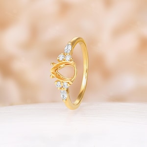 May include: A gold ring setting with a pear-shaped center stone and small round accent stones.