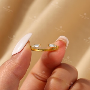 A close-up of a person's hand holding a gold ring with two small diamonds on the band.