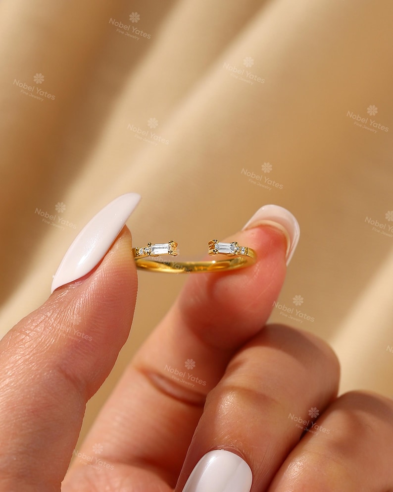 A close-up of a person's hand holding a gold ring with two small diamonds on the band.
