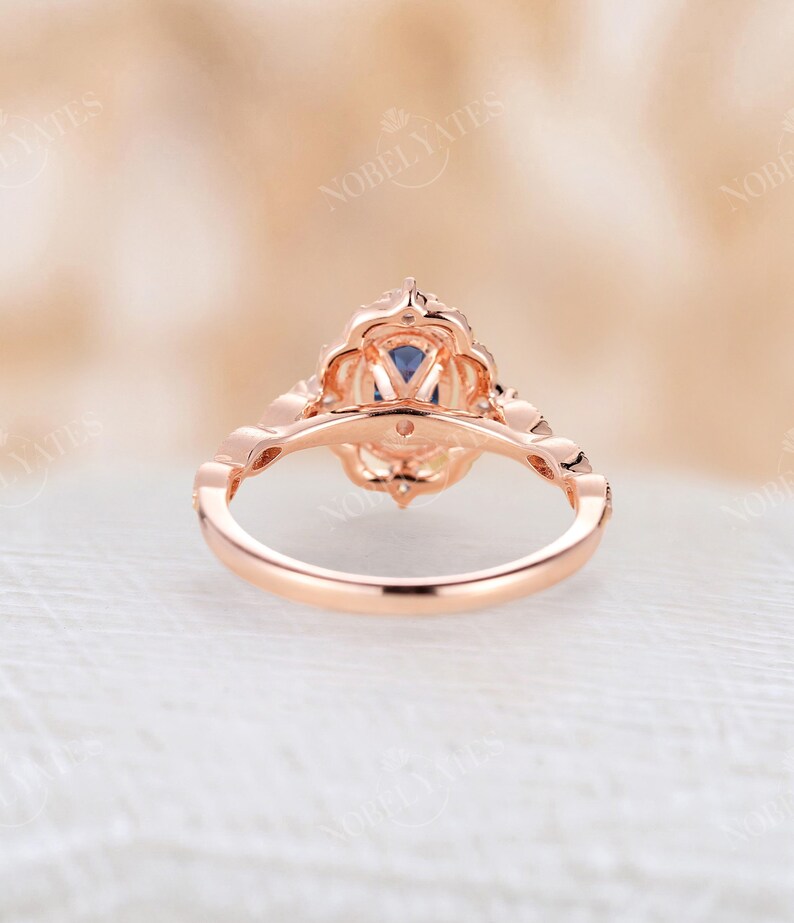 May include: A rose gold engagement ring with a blue gemstone surrounded by smaller white gemstones. The ring has a delicate, intricate design.