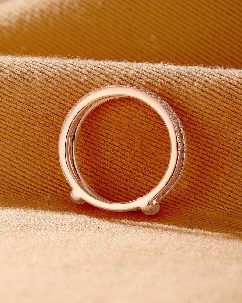 May include: A rose gold ring guard featuring a curved, open-ended design with a polished metal finish. The outer band is adorned with a row of small, clear pav&eacute;-set stones that extend along the top surface, creating a delicate and refined appearance.
