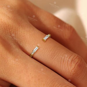 A close-up of a person's hand wearing a gold ring with two diamond-encrusted pieces.