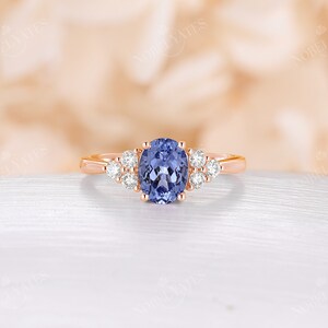 May include: A rose gold engagement ring with a large oval-shaped blue sapphire gemstone surrounded by smaller round diamonds.