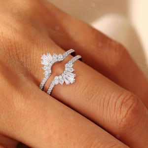 May include: A silver-toned ring guard featuring a curved design adorned with multiple small round-cut stones and two prominent baguette-cut stones at the ends. The band is encrusted with tiny pav&eacute;-set stones along the sides, creating a sparkling effect.