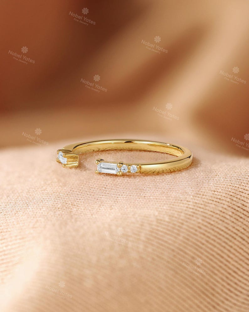 A gold ring with a diamond accent sits on a textured fabric surface.