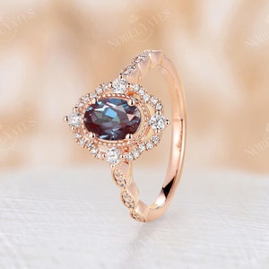 May include: A rose gold engagement ring with a large oval-shaped blue gemstone surrounded by a halo of smaller diamonds. The band is adorned with a row of smaller diamonds.