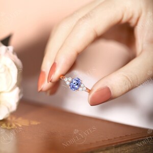 May include: A rose gold ring with a light blue oval gemstone surrounded by smaller clear gemstones.