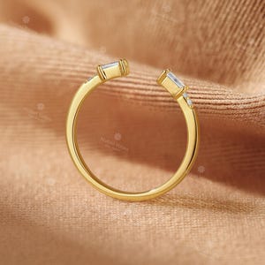 A gold ring with a unique design sits on a textured fabric surface.