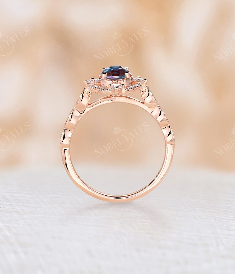 May include: A rose gold engagement ring with a halo setting featuring a blue gemstone surrounded by smaller clear gemstones. The band is adorned with a delicate, textured design.