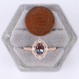 May include: A rose gold ring with a large oval alexandrite gemstone surrounded by a double halo of smaller diamonds. The ring is set in a delicate filigree design and is displayed in a gray velvet ring box.