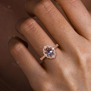 May include: A rose gold ring with a large oval-shaped gemstone surrounded by smaller diamonds. The ring is set in a delicate, ornate design.
