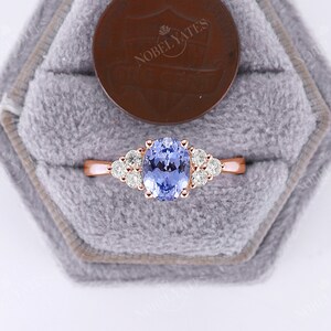 May include: A rose gold engagement ring with a light blue oval sapphire center stone and a halo of smaller round diamonds.