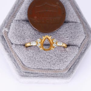 May include: A gold ring with a pear-shaped setting and small diamonds around the band. The ring is in a gray velvet ring box.