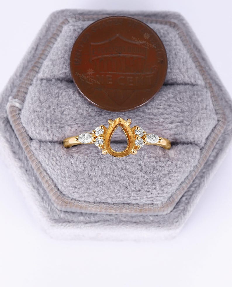 May include: A gold ring with a pear-shaped setting and small diamonds around the band. The ring is in a gray velvet ring box.