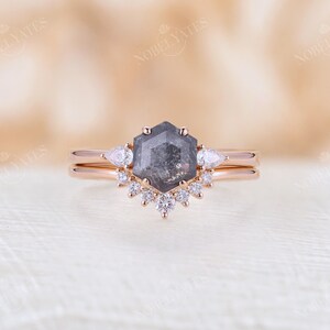Pode incluir: Um anel de noivado de ouro rosa com um diamante hexagonal cinza e um halo de diamantes menores. A banda tamb&eacute;m &eacute; de ouro rosa.