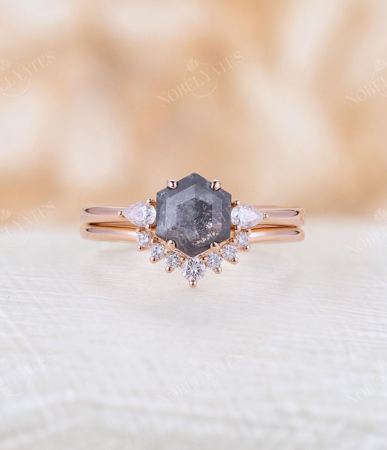 Pode incluir: Um anel de noivado de ouro rosa com um diamante hexagonal cinza e um halo de diamantes menores. A banda tamb&eacute;m &eacute; de ouro rosa.