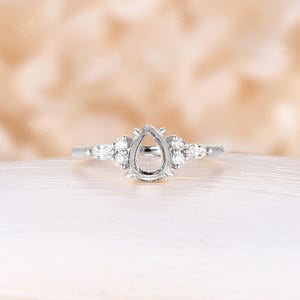 May include: A pear-shaped engagement ring setting with a delicate band and small accent diamonds.