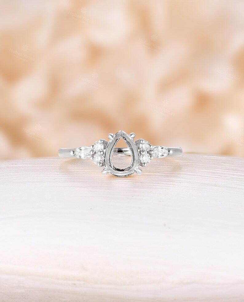 May include: A pear-shaped engagement ring setting with a delicate band and small accent diamonds.