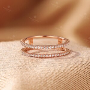 May include: A rose gold double band ring featuring two parallel bands connected by small vertical bars. Both bands are encrusted with a continuous row of small, clear, round-cut stones that catch the light, creating a delicate and refined appearance.
