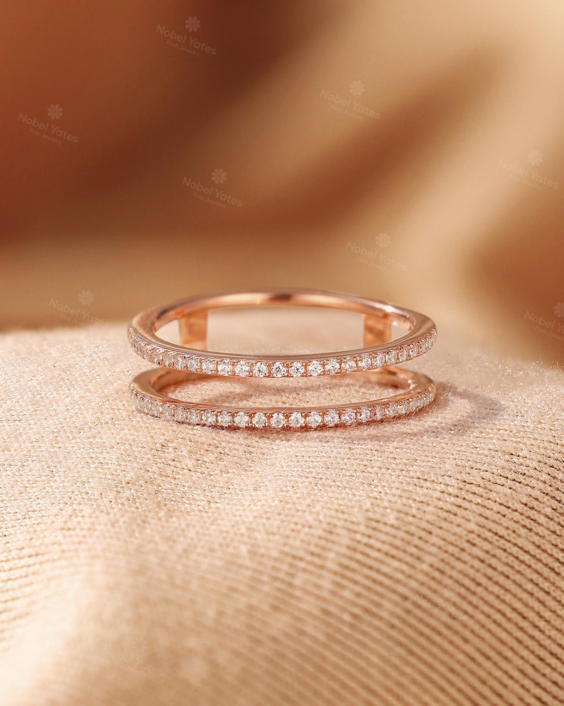 May include: A rose gold double band ring featuring two parallel bands connected by small vertical bars. Both bands are encrusted with a continuous row of small, clear, round-cut stones that catch the light, creating a delicate and refined appearance.