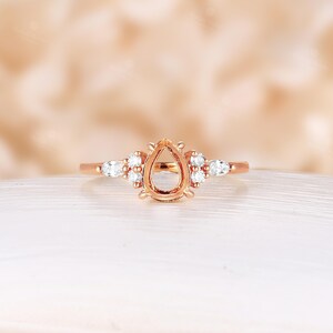 May include: A rose gold engagement ring setting with a pear-shaped center stone and small round diamonds on the band.