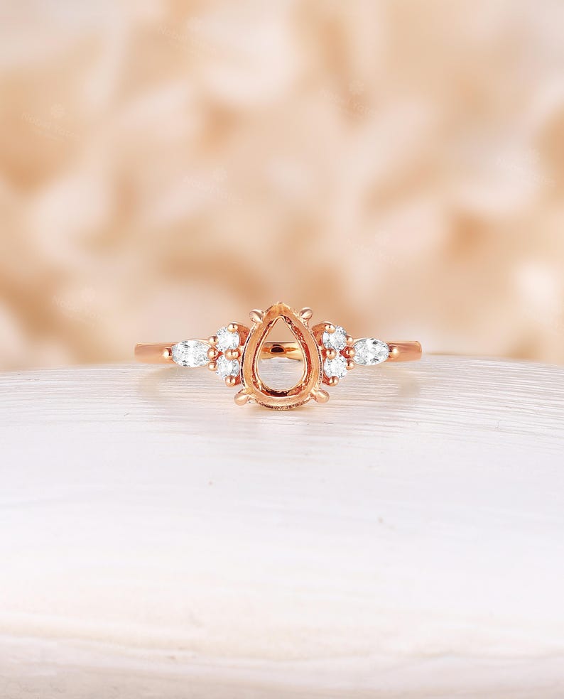 May include: A rose gold engagement ring setting with a pear-shaped center stone and small round diamonds on the band.