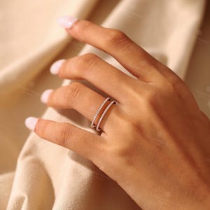 May include: A double band ring crafted from a metallic material, featuring two thin, parallel bands that are each set with a continuous row of small, clear, round-cut stones that catch the light, creating a delicate and refined appearance.