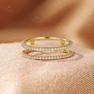 May include: A gold double-band ring featuring two parallel bands connected by small vertical bars. Both bands are encrusted with a continuous row of small, clear, round-cut pav&eacute;-set stones that extend around the entire circumference of the ring.