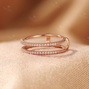 May include: A rose gold double band ring featuring two parallel bands connected by a small vertical bar. Both bands are encrusted with a row of small, clear, round-cut stones along the outer surface, creating a delicate and refined appearance.
