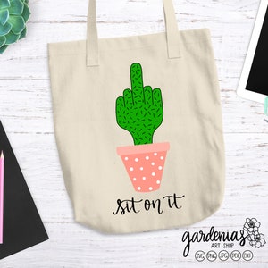 May include: A white tote bag with a green cactus giving the middle finger. The cactus is in a pink pot with white polka dots. The text "sit on it" is written below the cactus.