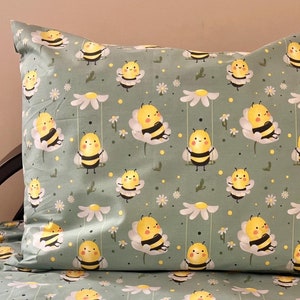 Può includere: Un lenzuolo da letto verde e bianco con un motivo di api gialle su margherite bianche. Il lenzuolo è su un letto con una federa abbinata.