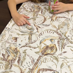 Puede incluir: Un camino de mesa blanco con estampado de faisanes marrones y verdes. El camino de mesa presenta un patrón repetitivo de faisanes, hojas y ramas.