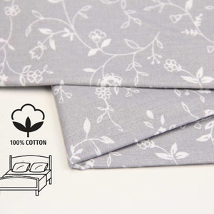 May include: Gray cotton fabric with a white floral pattern. The fabric is folded in half and shows the pattern on both sides. The fabric is 100% cotton and is suitable for making bedding.