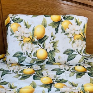 May include: Bed linen set with a lemon and floral design. The pattern showcases yellow lemons, white flowers, and green foliage on a white background. The set includes a pillowcase and a sheet, ideal for a fresh bedroom aesthetic.