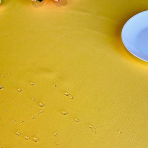 Puede incluir: Un mantel amarillo con gotas de agua en la superficie. El mantel es liso y tiene una textura sutil.