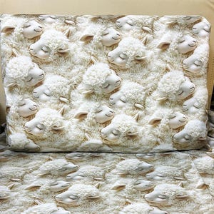 May include: Cream-coloured bedding set with a repeating pattern of fluffy, white sheep with closed eyes. The sheep have detailed faces and are set against a textured background, creating a cosy and whimsical design.