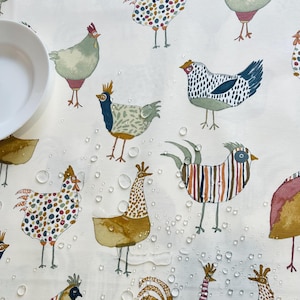 May include: A white tablecloth featuring a repeating pattern of colorful, whimsical chickens and roosters. The illustrations include various patterns and colors, with water droplets scattered across the surface. A white plate is visible in the upper left corner.