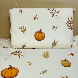 Op de afbeelding: Witte beddengoedset met een herhalend patroon van oranje pompoenen en herfstbladeren in bruin- en goudtinten. De set bevat een kussensloop en een laken, perfect voor herfstdecoratie.
