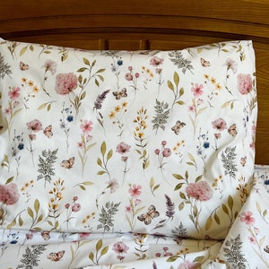 May include: A white bedding set with a floral pattern featuring pink and yellow flowers, green leaves, and butterflies. The bedding is made of soft, comfortable fabric and is perfect for adding a touch of nature to your bedroom.