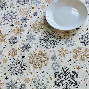 Könnte beinhalten: Weißer Tischläufer mit einem Schneeflockenmuster in Schwarz, Gold und Grau. Der Tischläufer ist mit Wassertropfen bedeckt.