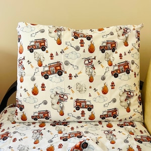 May include: White bedding with a fire truck and helicopter pattern. The bedding features red fire trucks, orange flames, and gray smoke. The words "FIRE" are repeated throughout the pattern.
