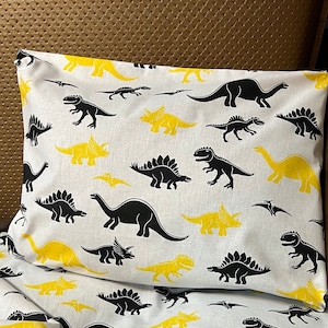 May include: White bedding with a black and yellow dinosaur print. The bedding features a variety of dinosaur silhouettes, including stegosaurus, brachiosaurus, and triceratops.