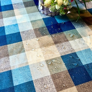 Puede incluir: Un mantel de mesa a cuadros azules y marrones con gotas de agua en la superficie. El mantel está hecho de tela tejida y tiene una textura sutil.